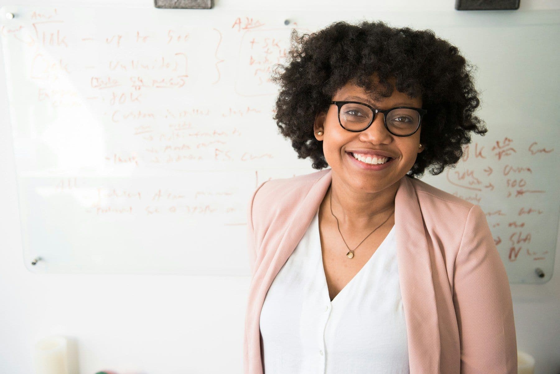 A smiling Black woman educator in front of a whiteboard