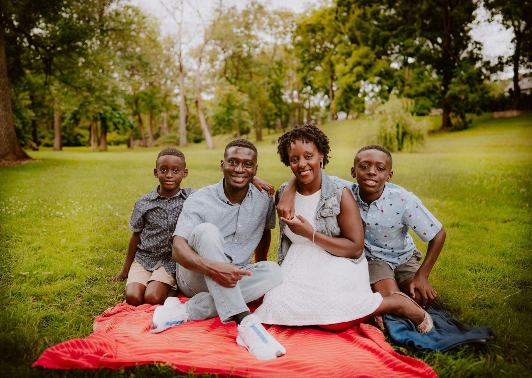 A Black family relaxing together on a picnic blanket in a green park