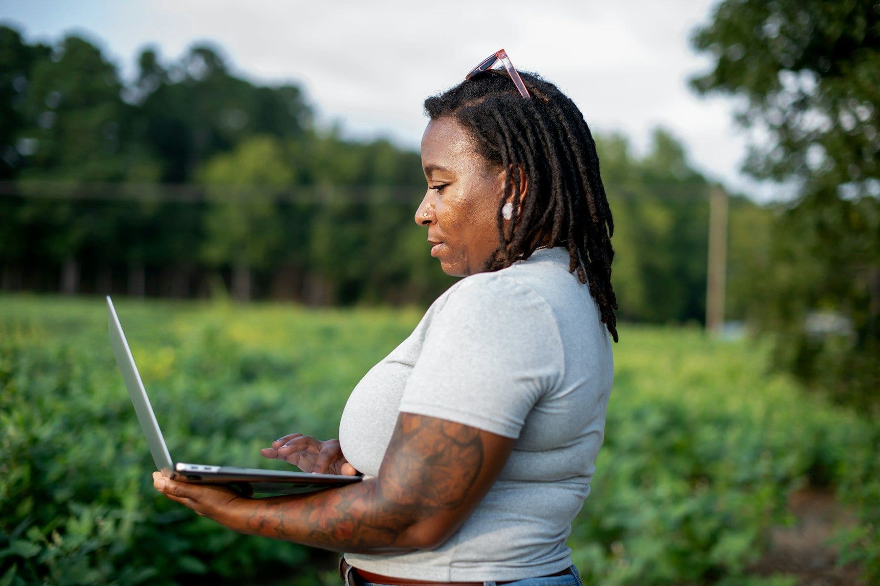 A woman with locs reviewing data on a laptop in a green field