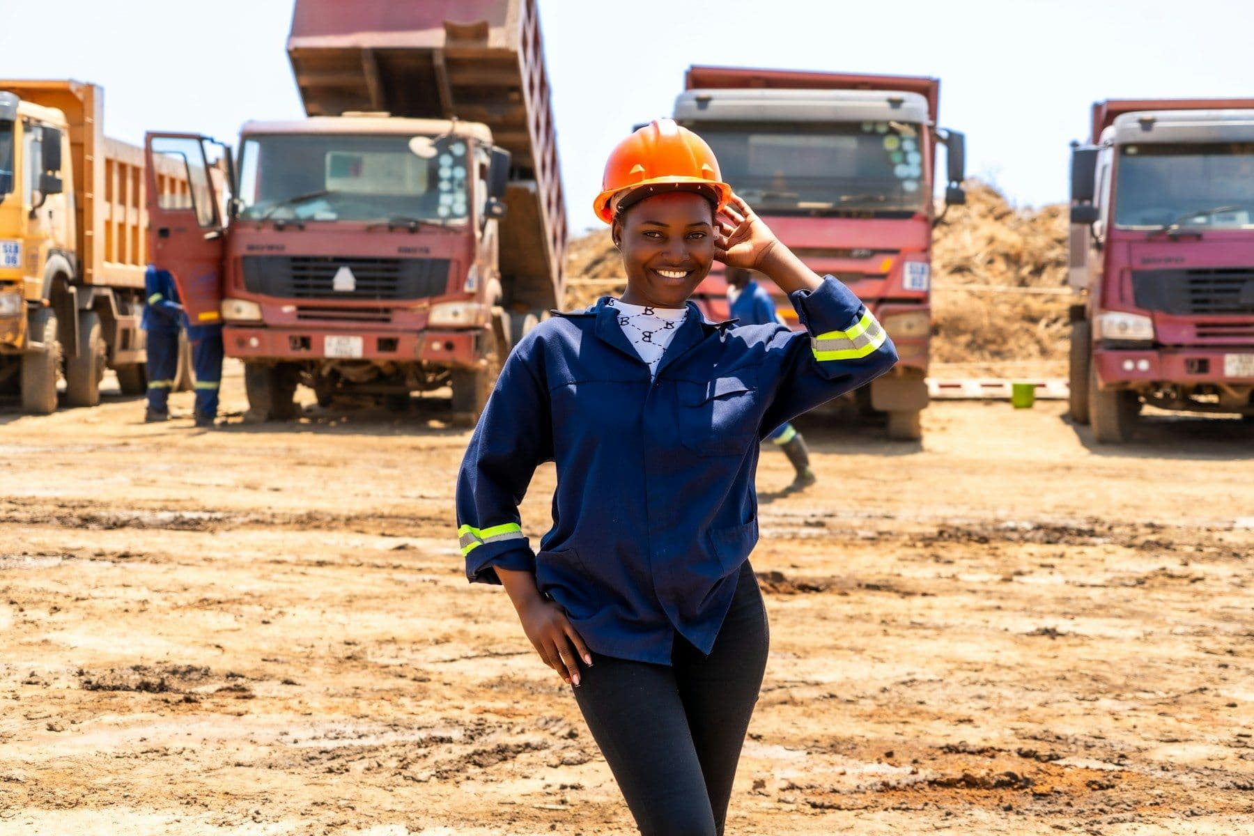 A smiling young woman in workwear and a hard hat on a worksite
